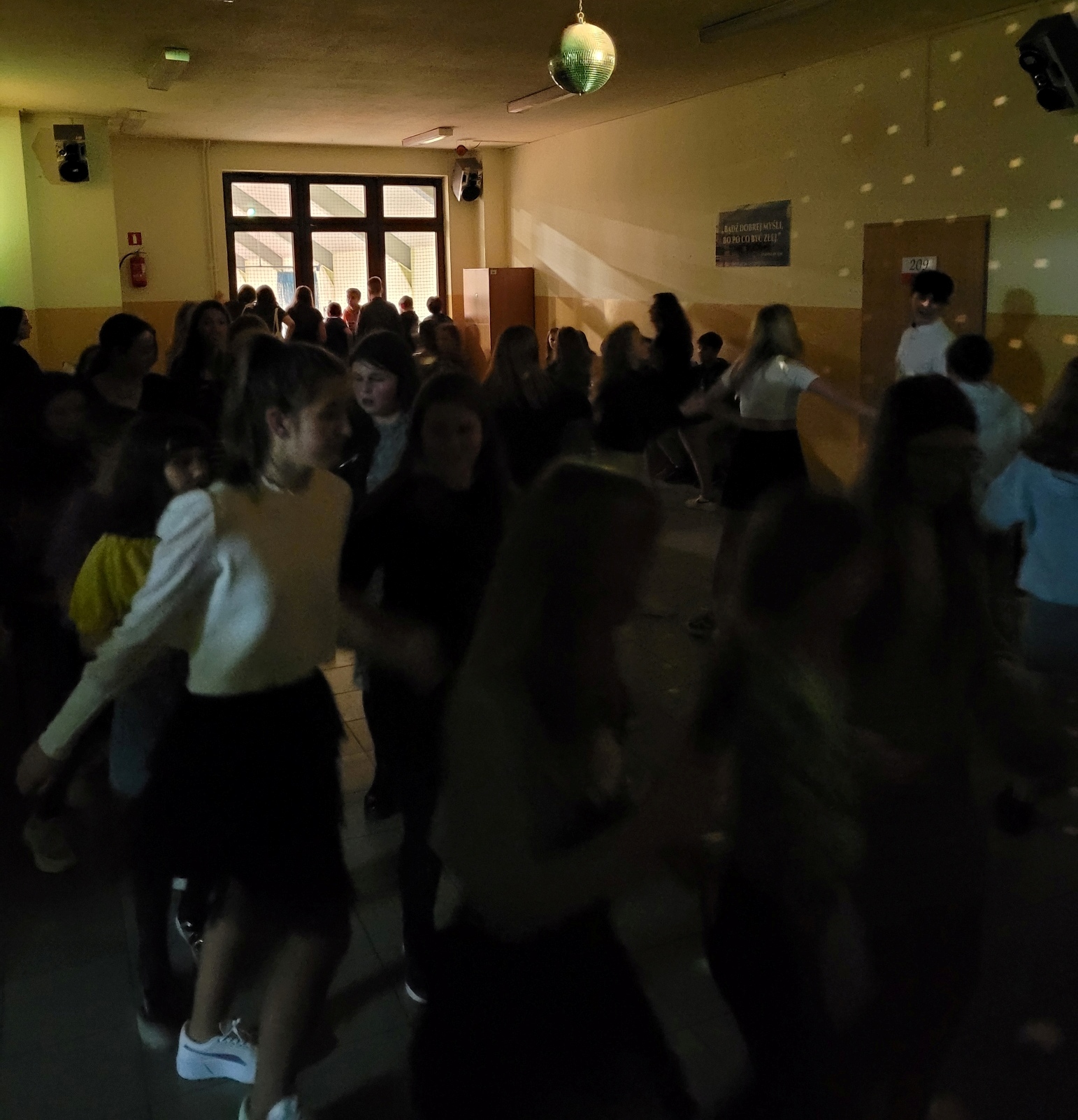Na zdjęciu widzimy tańczącą młodzież na szkolnym korytarzu.