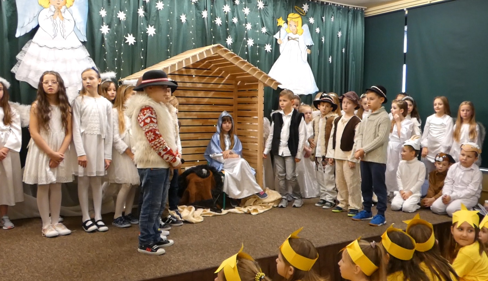 Uczniowie klas I-III  przedstawiają jasełka na tle szopki. Dzieci są przebrane w stroje aniołów, pastuszków, zwierząt.