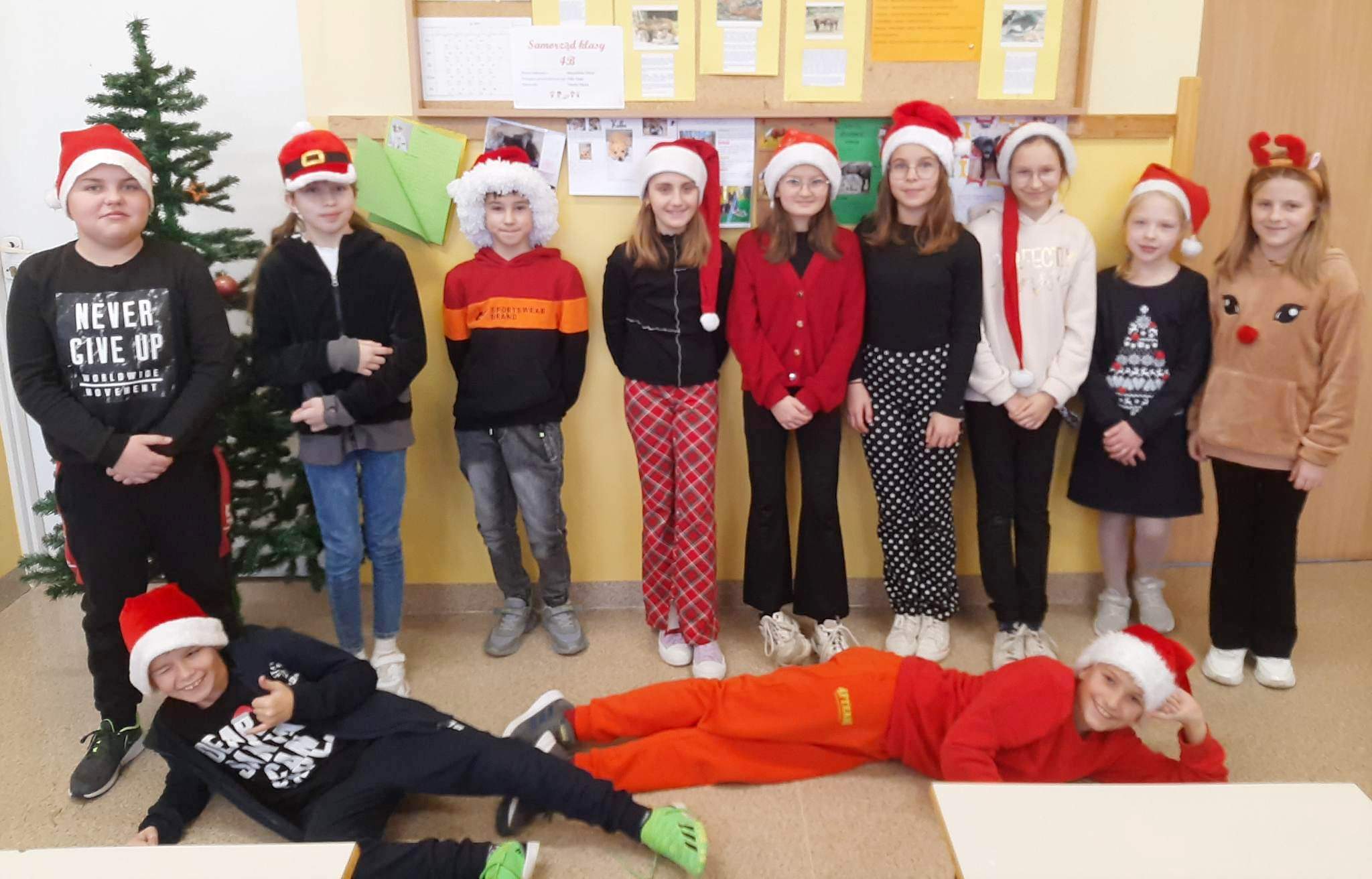 Grupa dzieci ubranych w czapki Mikołaja stojących w sali lekcyjnej.