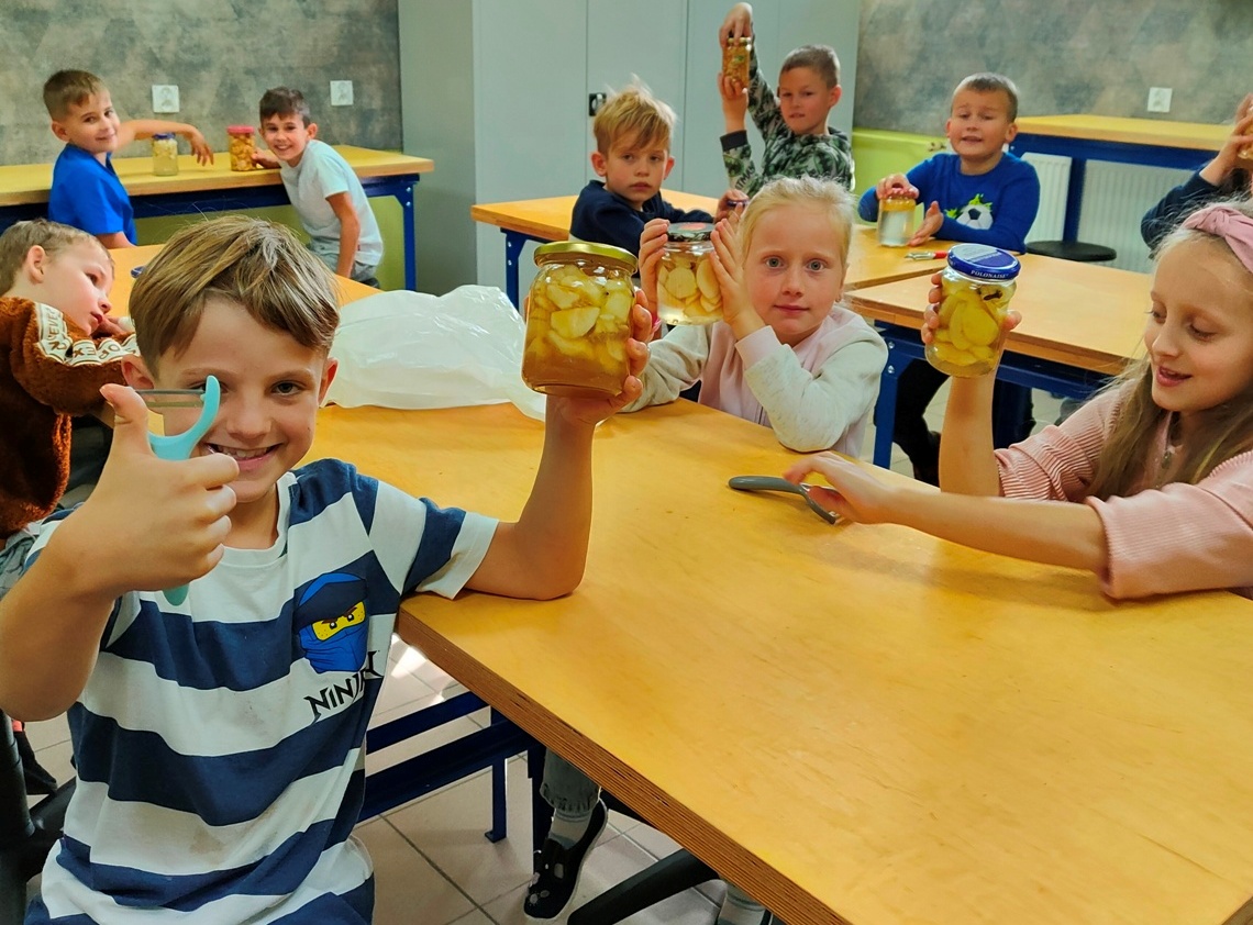 Zadowolone dzieci prezentują słoiki wypełnione gruszkami w syropie.