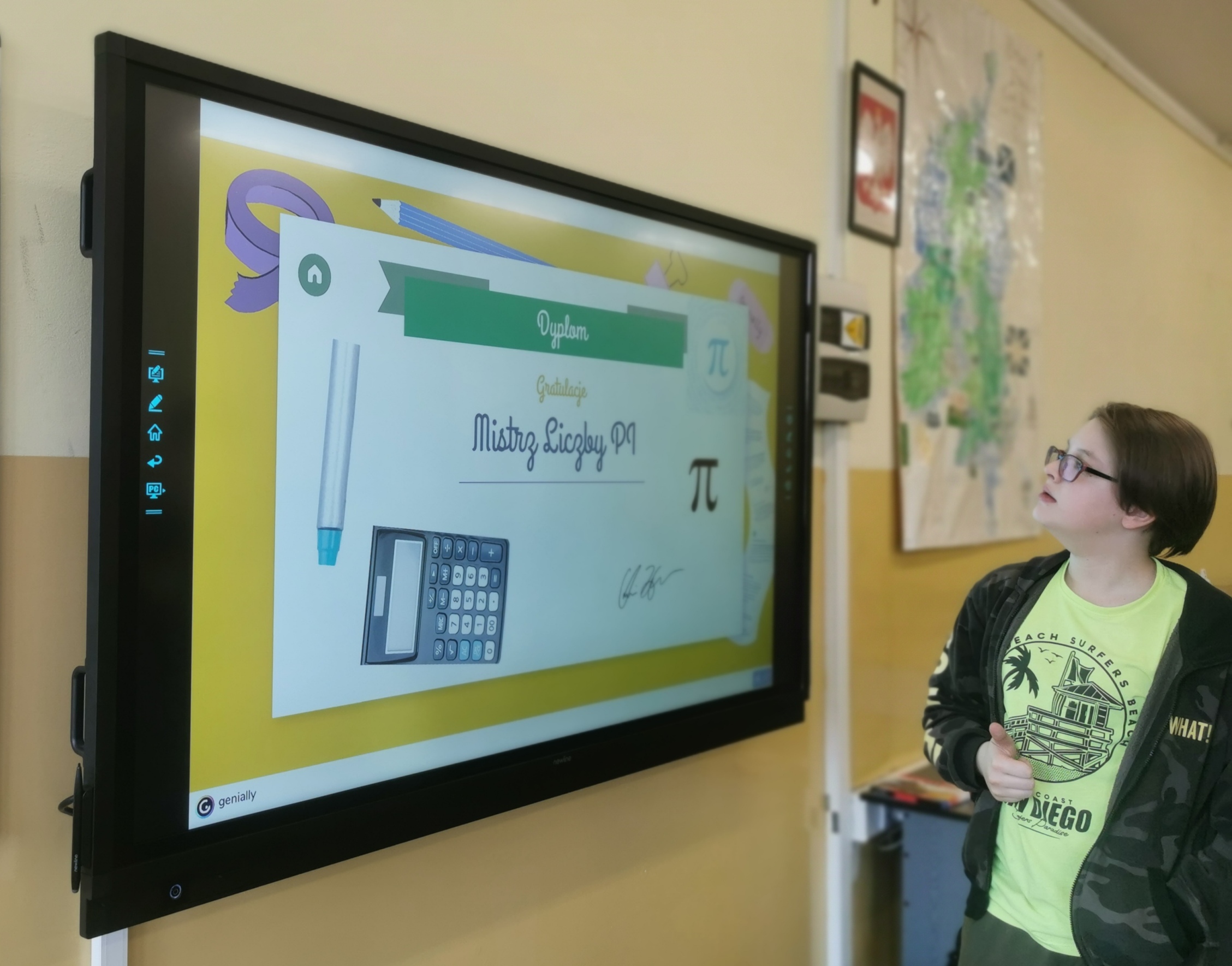 Zdjęcie przedstawia ucznia, który stoi przed tablicą multimedialną  z grą edukacyjną na temat liczby Pi